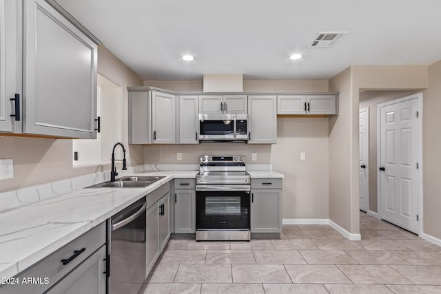 kitchen with light stone countertops, gray cabinetry, stainless steel appliances, sink, and light tile patterned floors