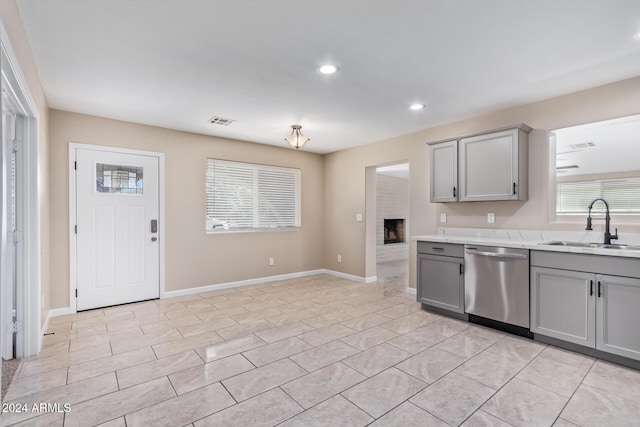 kitchen featuring stainless steel dishwasher, sink, a fireplace, gray cabinets, and light tile patterned flooring