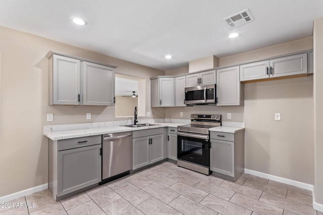 kitchen with gray cabinetry, light stone countertops, sink, light tile patterned floors, and appliances with stainless steel finishes