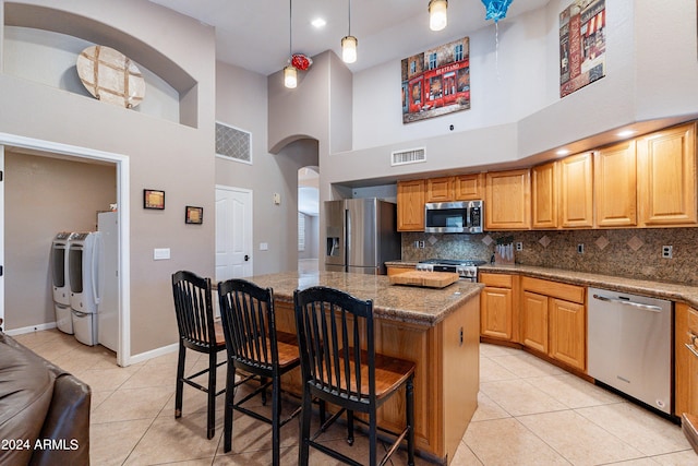 kitchen with a center island, stainless steel appliances, a high ceiling, pendant lighting, and washer and clothes dryer