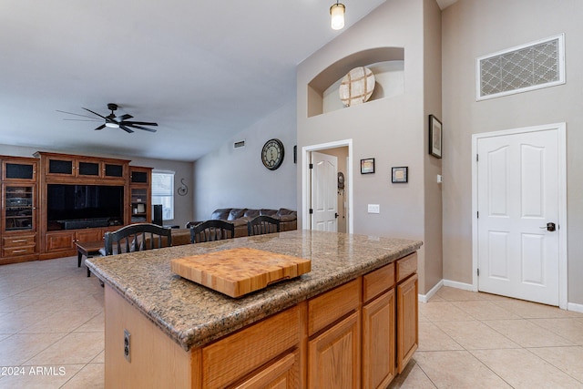 kitchen with stone counters, ceiling fan, a kitchen island, and light tile patterned flooring