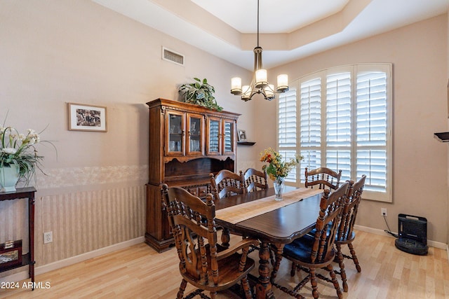 dining area featuring a tray ceiling, a chandelier, and light hardwood / wood-style floors