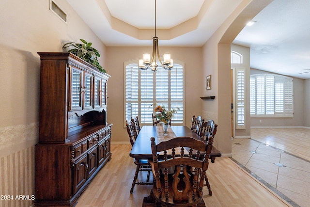 dining area with a raised ceiling, a wealth of natural light, and light hardwood / wood-style floors