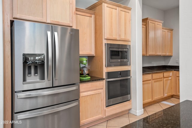 kitchen with light brown cabinets, stainless steel appliances, light tile patterned floors, and dark stone counters