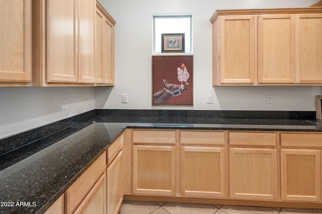 kitchen with dark stone countertops, light brown cabinets, and light tile patterned floors