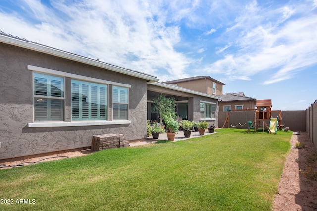 rear view of property featuring a playground and a lawn