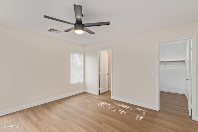 unfurnished bedroom featuring baseboards, visible vents, light wood-style flooring, a closet, and a walk in closet