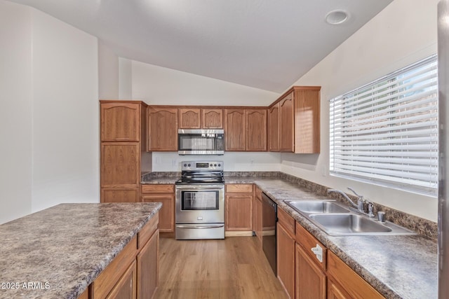 kitchen featuring vaulted ceiling, light wood-style flooring, appliances with stainless steel finishes, brown cabinetry, and a sink