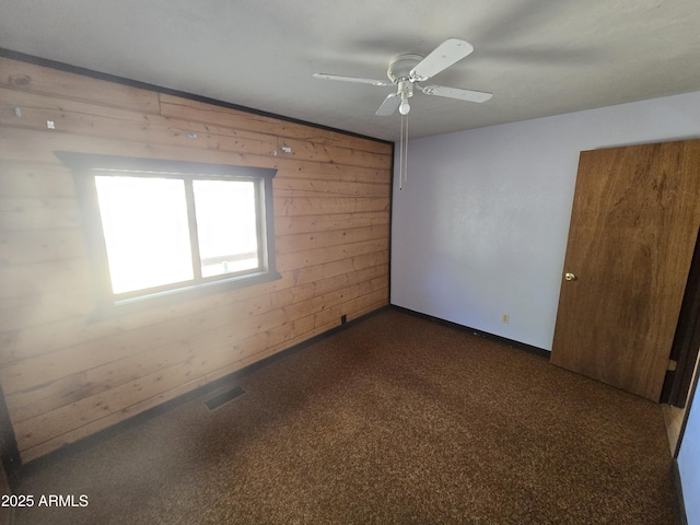 spare room with a ceiling fan, visible vents, wooden walls, and baseboards