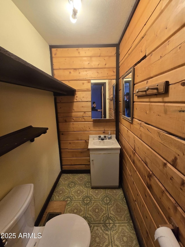 bathroom featuring wooden walls, baseboards, visible vents, toilet, and vanity