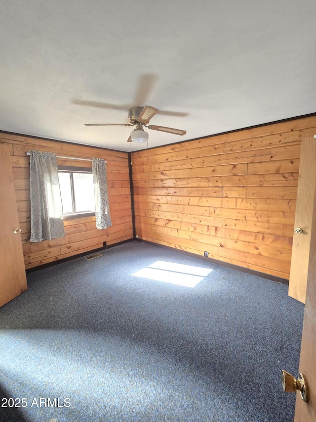 unfurnished room featuring visible vents, carpet, a ceiling fan, and wooden walls