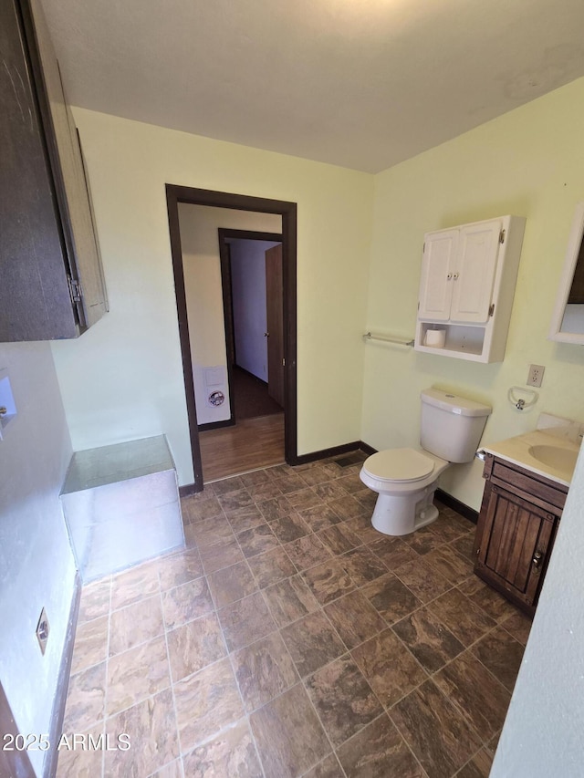 bathroom featuring stone finish floor, toilet, vanity, and baseboards