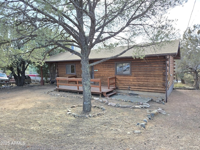 exterior space with a deck, log exterior, and a shingled roof