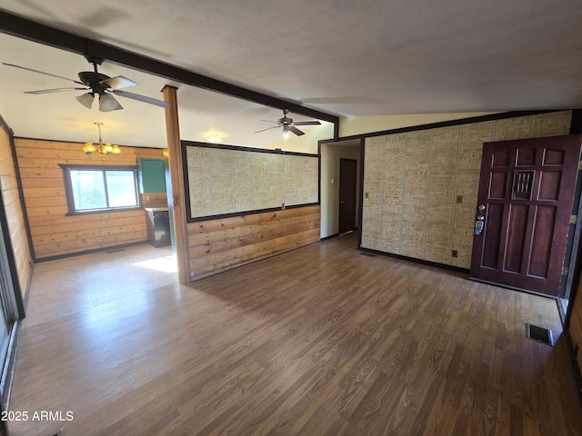 unfurnished living room featuring visible vents, lofted ceiling with beams, wood walls, wood finished floors, and ceiling fan with notable chandelier