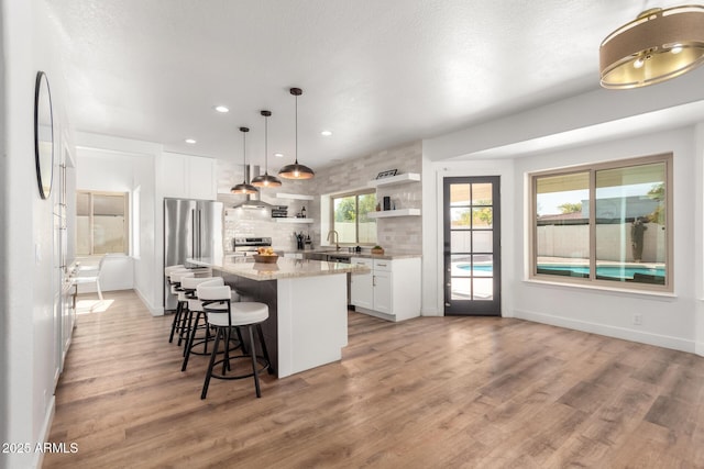 kitchen with decorative light fixtures, a kitchen island, white cabinets, light stone countertops, and backsplash