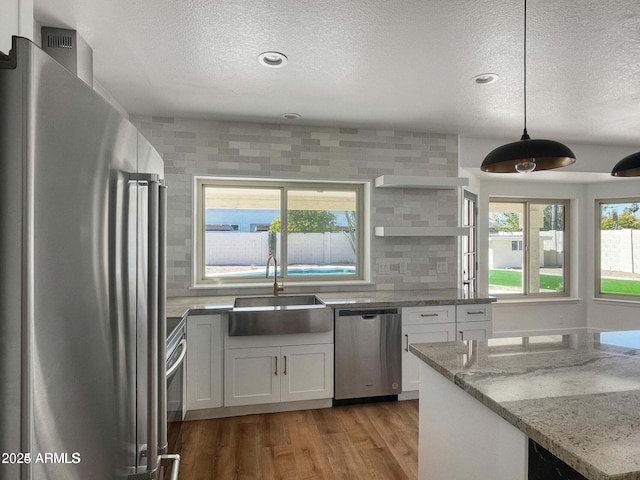 kitchen with sink, appliances with stainless steel finishes, white cabinetry, hanging light fixtures, and light stone countertops