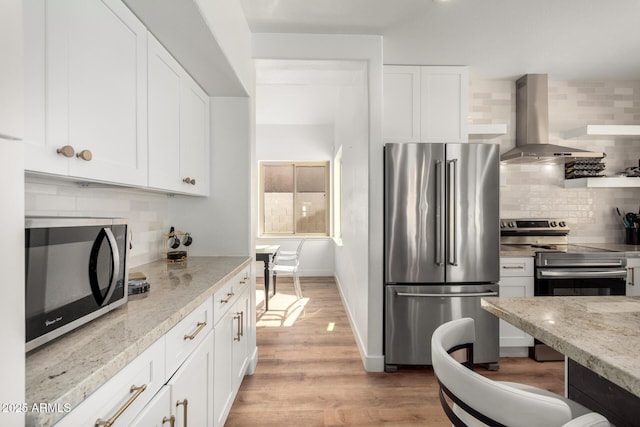 kitchen featuring white cabinetry, appliances with stainless steel finishes, light stone counters, and wall chimney exhaust hood