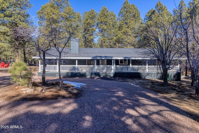 view of front of home featuring gravel driveway, a chimney, and a porch