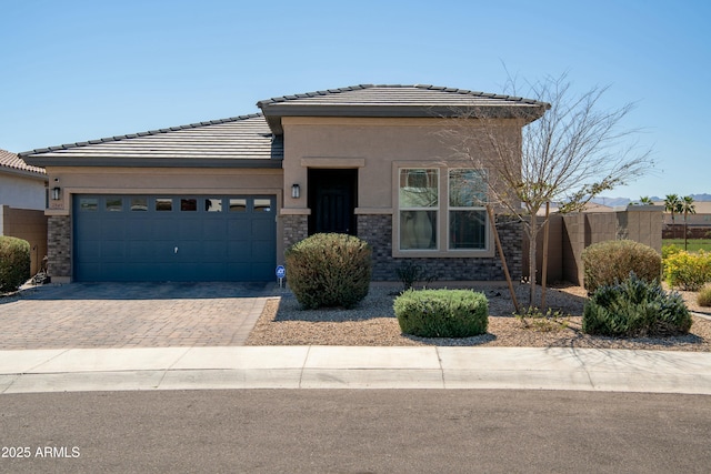 prairie-style house featuring stucco siding, a tile roof, decorative driveway, fence, and a garage