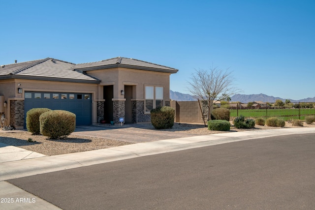 view of front facade with stucco siding, stone siding, fence, a mountain view, and a garage