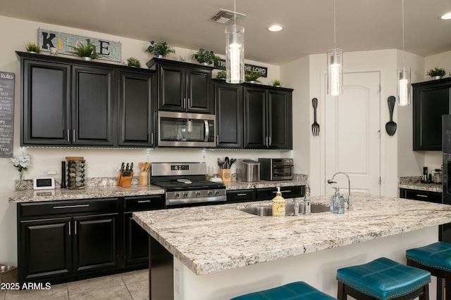 kitchen featuring appliances with stainless steel finishes, dark cabinetry, a kitchen breakfast bar, and a sink