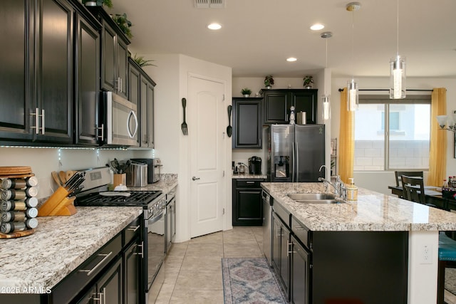 kitchen featuring a center island with sink, a sink, decorative light fixtures, dark cabinetry, and appliances with stainless steel finishes