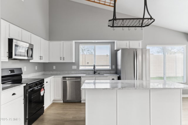 kitchen with sink, stainless steel appliances, light stone counters, white cabinets, and a kitchen island