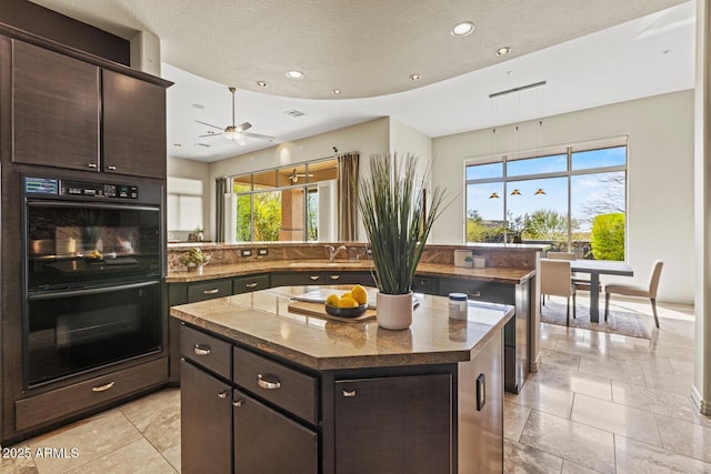 kitchen featuring a sink, dobule oven black, plenty of natural light, and a center island