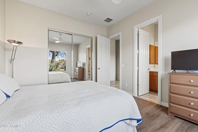 bedroom featuring visible vents, baseboards, ensuite bathroom, wood finished floors, and a closet
