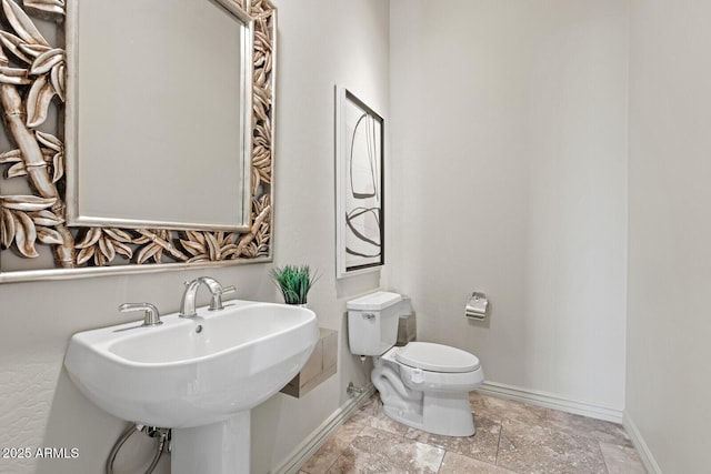 bathroom featuring a sink, baseboards, toilet, and stone finish floor