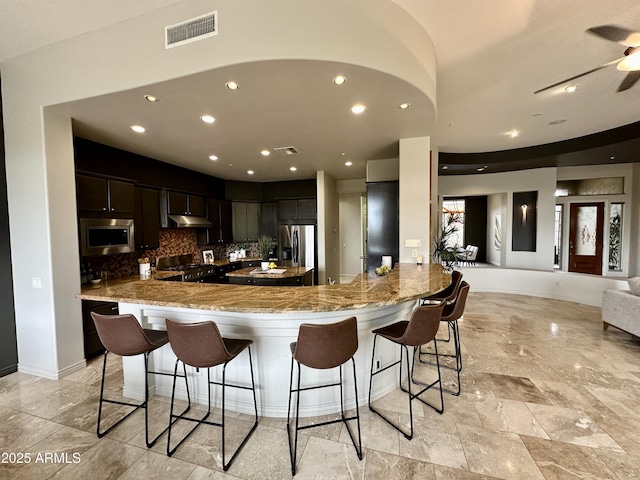 kitchen with under cabinet range hood, visible vents, appliances with stainless steel finishes, and a breakfast bar area