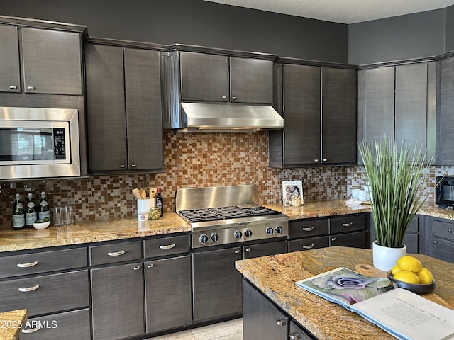 kitchen with under cabinet range hood, decorative backsplash, light stone counters, and appliances with stainless steel finishes