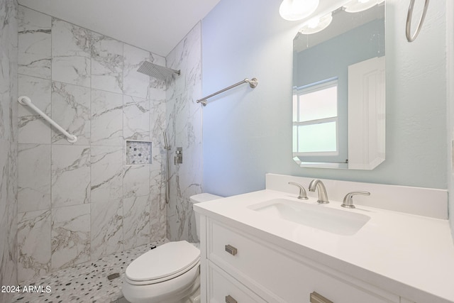 bathroom with toilet, a tile shower, and vanity