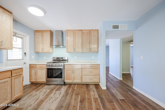 kitchen with light brown cabinets, stainless steel range with gas stovetop, wall chimney exhaust hood, and light hardwood / wood-style flooring