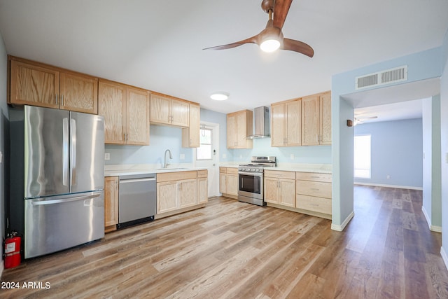 kitchen with light hardwood / wood-style flooring, appliances with stainless steel finishes, sink, wall chimney range hood, and ceiling fan