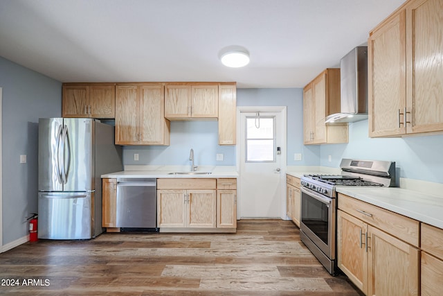 kitchen featuring stainless steel appliances, sink, wall chimney exhaust hood, light brown cabinets, and light hardwood / wood-style floors