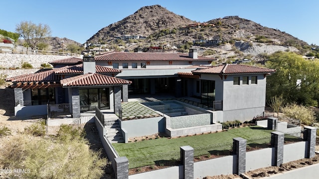 back of house with a fenced front yard, a tile roof, a mountain view, and a yard