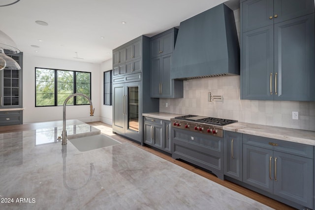 kitchen with decorative backsplash, stainless steel gas cooktop, wall chimney range hood, and a sink