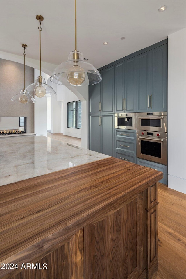 kitchen with arched walkways, light stone counters, wood finished floors, hanging light fixtures, and double oven