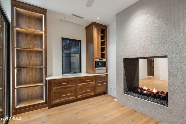 bar featuring ceiling fan, a multi sided fireplace, oven, and light hardwood / wood-style flooring