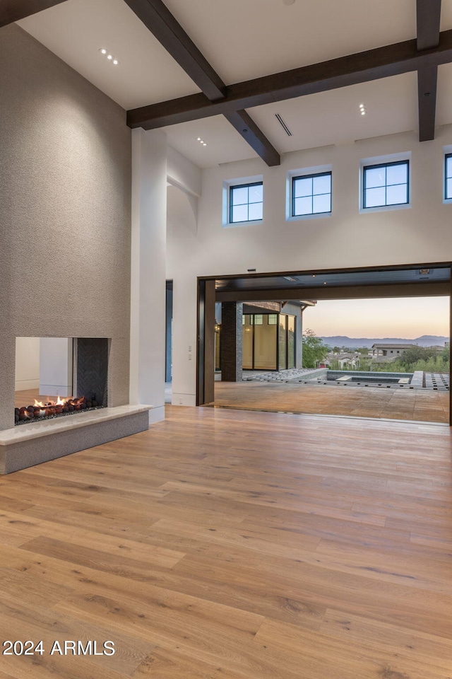 unfurnished living room with beam ceiling, light hardwood / wood-style flooring, a high ceiling, and a multi sided fireplace