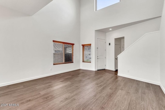 unfurnished living room featuring baseboards, a high ceiling, and wood finished floors