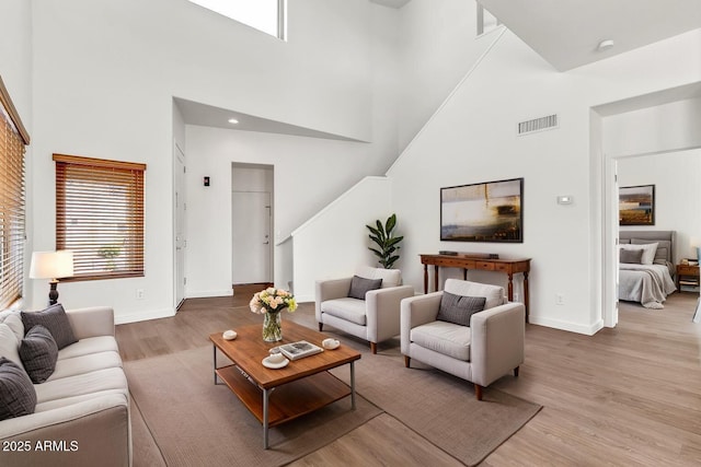 living room with baseboards, visible vents, wood finished floors, and a towering ceiling