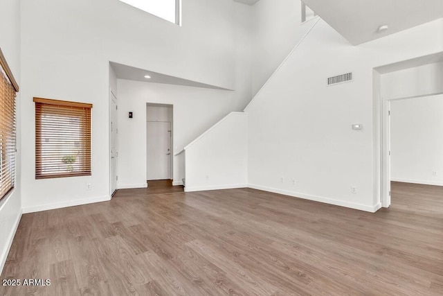 unfurnished living room with baseboards, a high ceiling, visible vents, and wood finished floors
