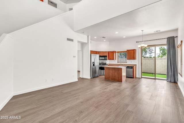 kitchen featuring stainless steel appliances, visible vents, brown cabinetry, and a center island