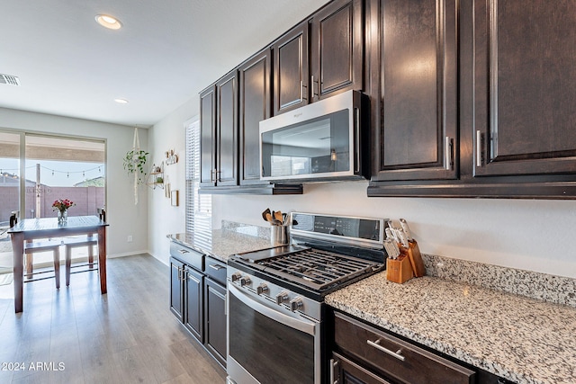 kitchen featuring light stone countertops, appliances with stainless steel finishes, dark brown cabinetry, and light hardwood / wood-style floors