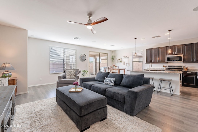 living room featuring ceiling fan, light wood-type flooring, and sink