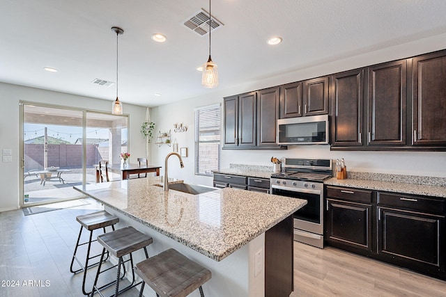 kitchen featuring sink, stainless steel appliances, hanging light fixtures, and an island with sink