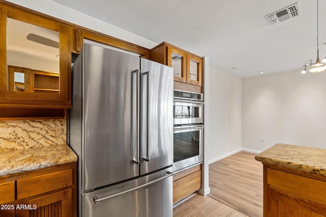 4200 N Miller Rd Unit 504, Scottsdale, AZ 85251 - kitchen with appliances with stainless steel finishes, brown cabinets, glass insert cabinets, and light stone counters