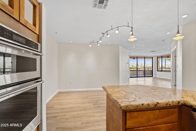 4200 N Miller Rd Unit 504, Scottsdale, AZ 85251 - kitchen featuring stainless steel double oven, brown cabinetry, light stone counters, light wood-style floors, and recessed lighting